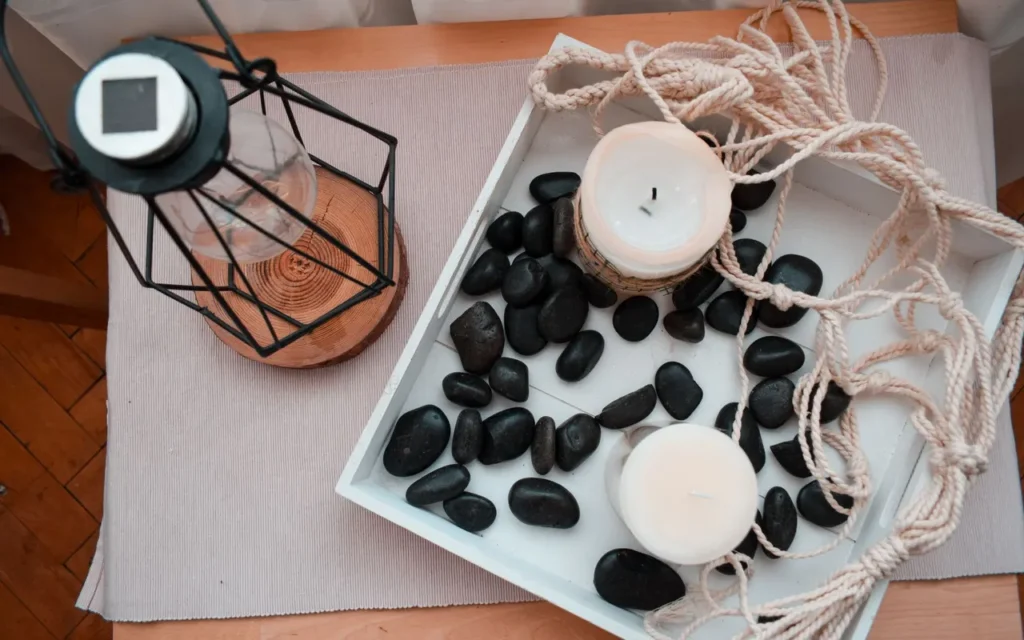 Candles, black stones and a metal lantern on a wooden tray