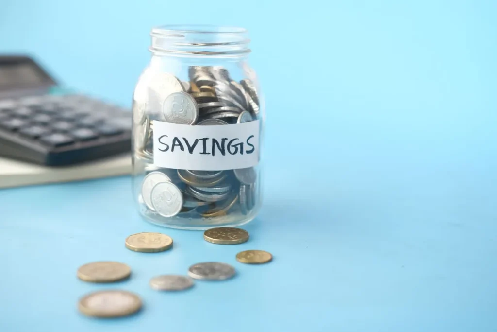 Glass jar labelled savings with coins beside it