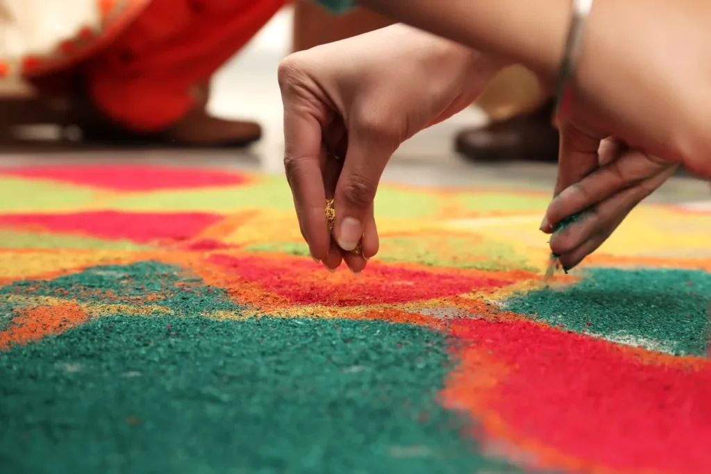 Hands creating a colourful rangoli pattern with powder