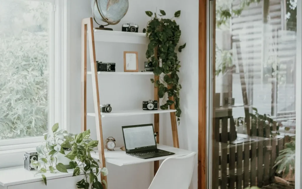 Home office desk surrounded by trailing houseplants by a window