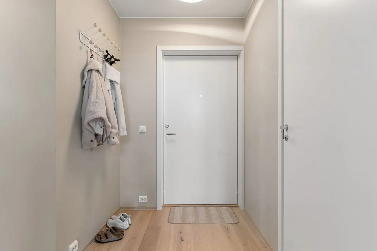 Minimalist apartment entrance with a white front door and coat hooks