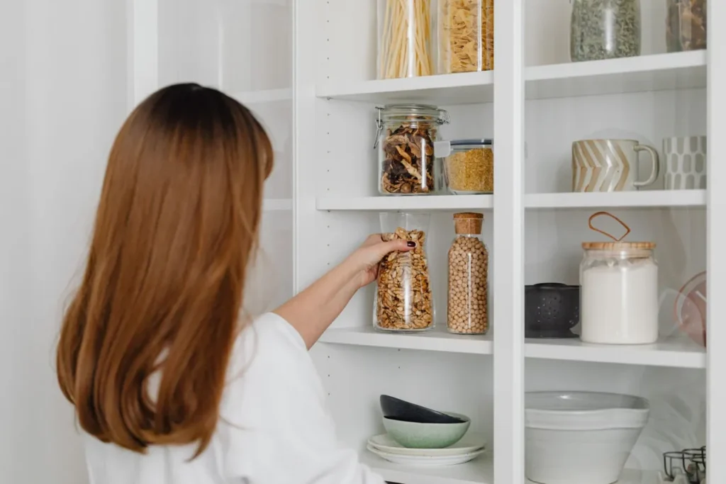 Woman organising jars on open kitchen shelves
