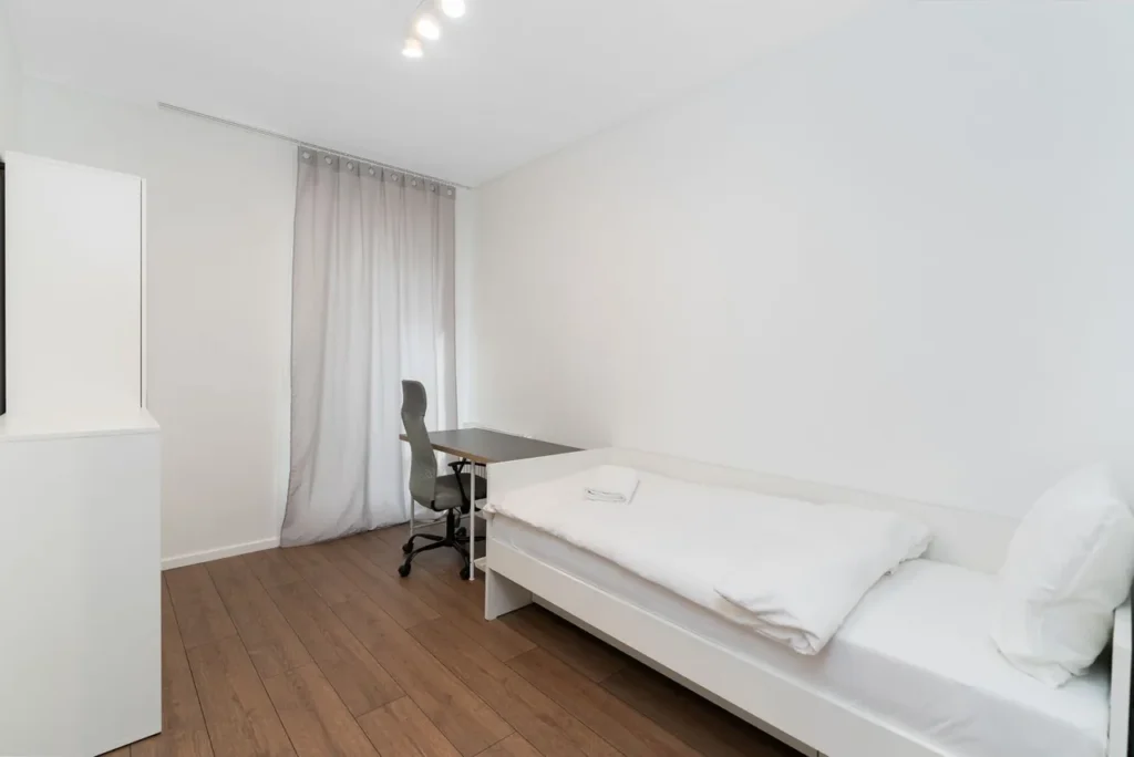 Small bright bedroom with a single bed against a solid white wall