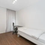 Small bright bedroom with a single bed against a solid white wall