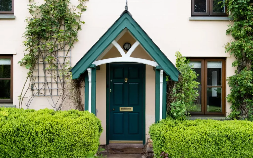 Teal front door under a small gabled porch with hedges
